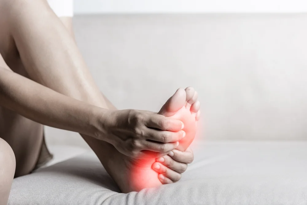 A person massages their foot, with areas of red indicating pain in the heel and sole, suggesting when to see a podiatrist for heel pain.